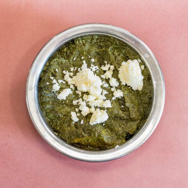 Overhead view of a metal bowl filled with green saag, topped with crumbled white paneer cheese.