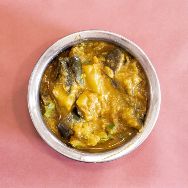 Top-down view of a silver bowl filled with a yellow curry containing potatoes and green vegetables.