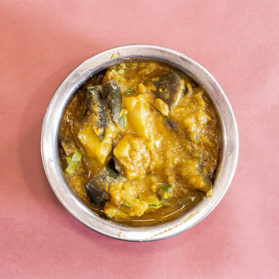 Top-down view of a silver bowl filled with a yellow curry containing potatoes and green vegetables.