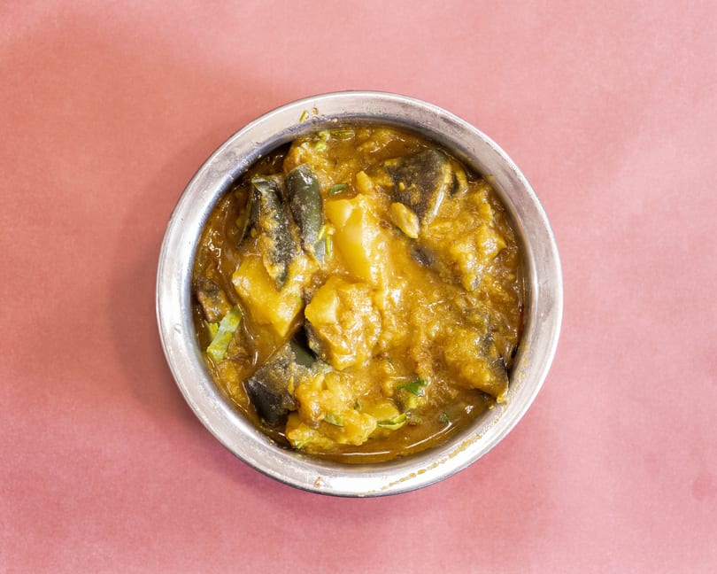 Top-down view of a silver bowl filled with a yellow curry containing potatoes and green vegetables.