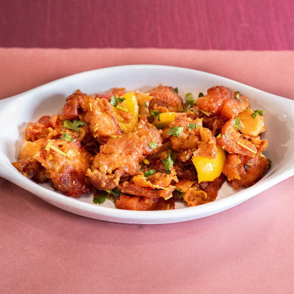 Crispy fried chicken with yellow bell peppers and cilantro in a white dish.