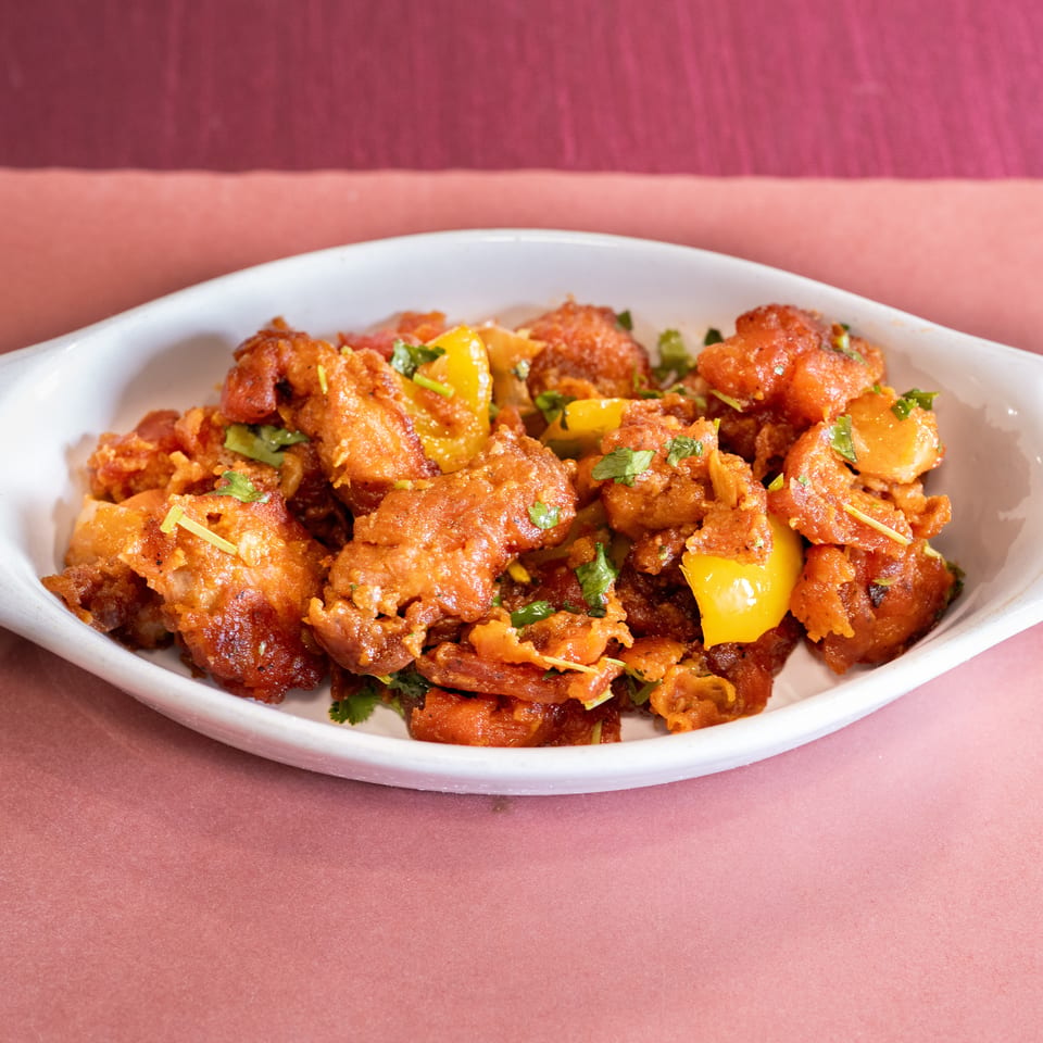 Crispy fried chicken with yellow bell peppers and cilantro in a white dish.