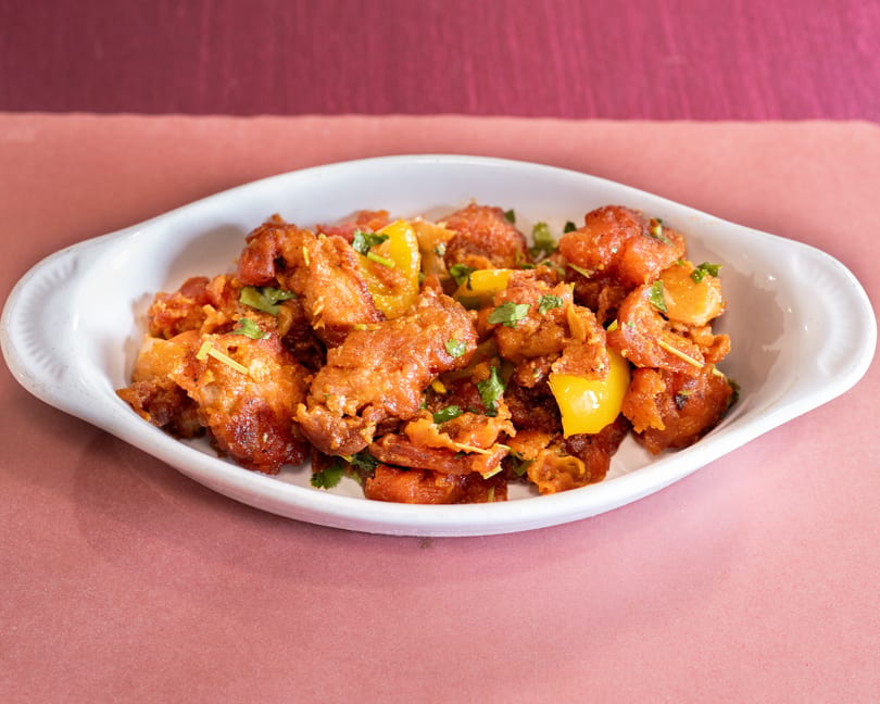 Crispy fried chicken with yellow bell peppers and cilantro in a white dish.