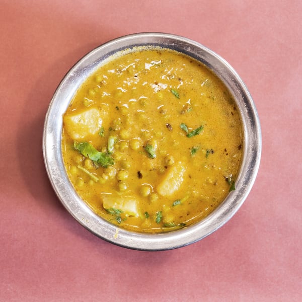 Overhead view of a metal bowl filled with a yellow curry, potatoes, and green peas.