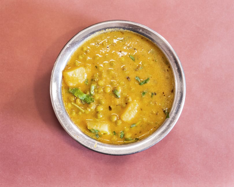 Overhead view of a metal bowl filled with a yellow curry, potatoes, and green peas.