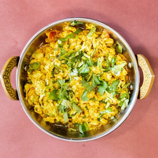 Scrambled paneer with spices and fresh cilantro in a metal karahi on a pink surface.